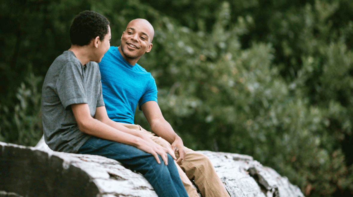 a father and son talk on a rock outside, looking for growth opportunities in challenges