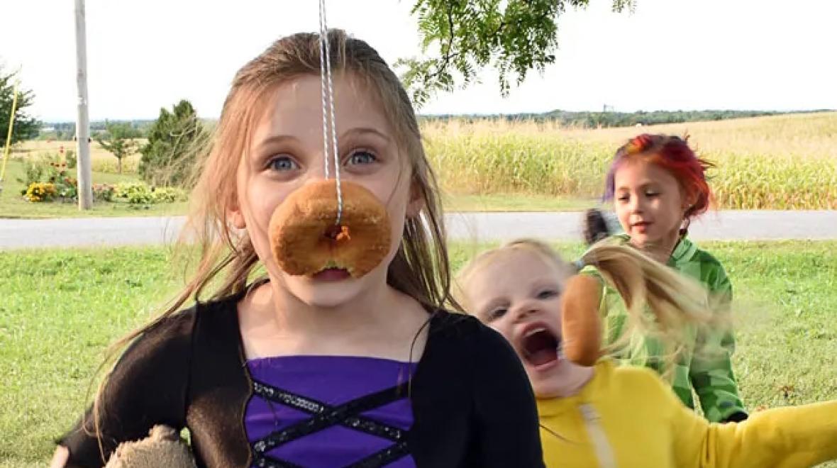 Girl eating a donut on a string is a delicious Halloween party game kids love to play