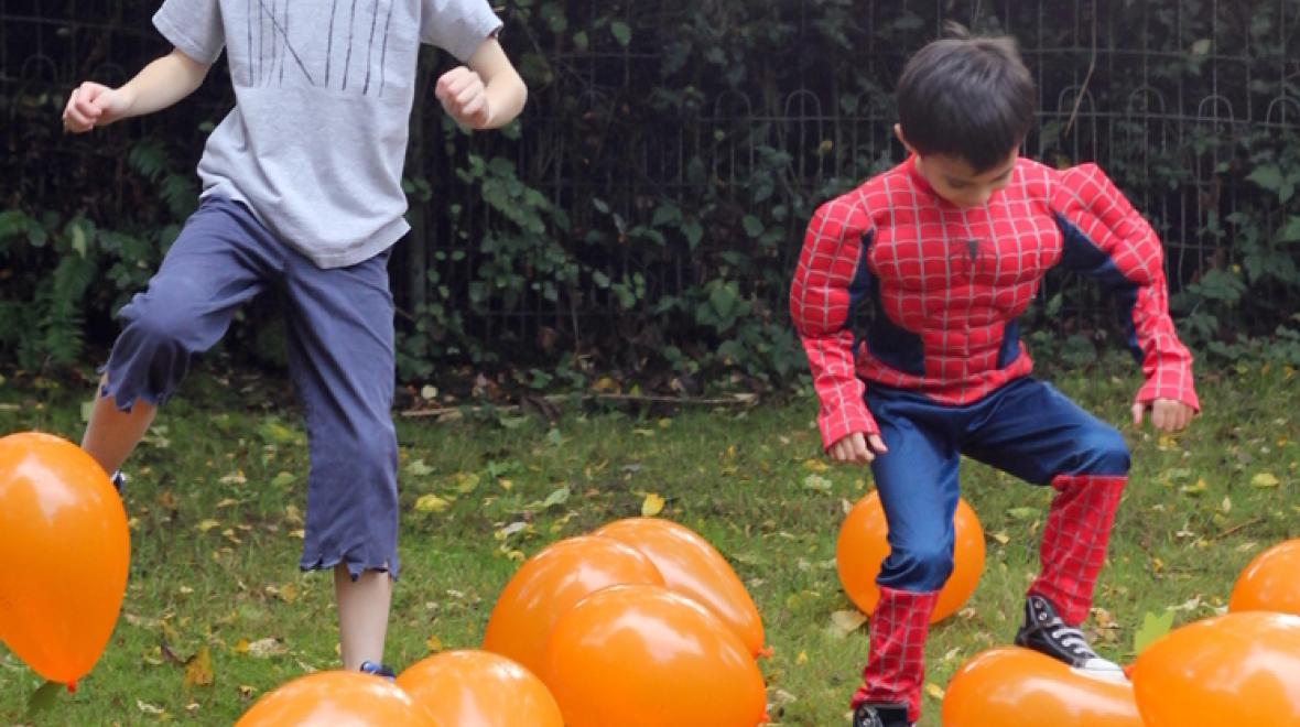 Two boys in Halloween costumes stomping on balloons as part of a Halloween party game for kids