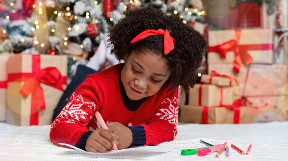 Young girl writing a letter to Santa under a Christmas tree