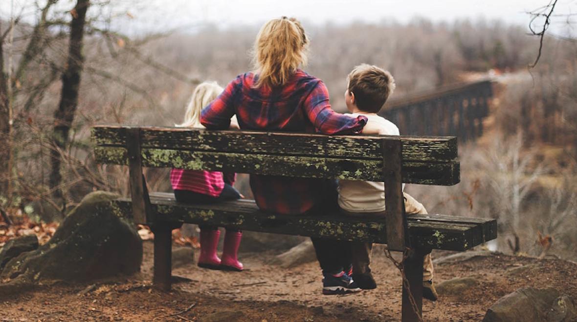 Mom with two children sitting on a bench outside facing away from the camera