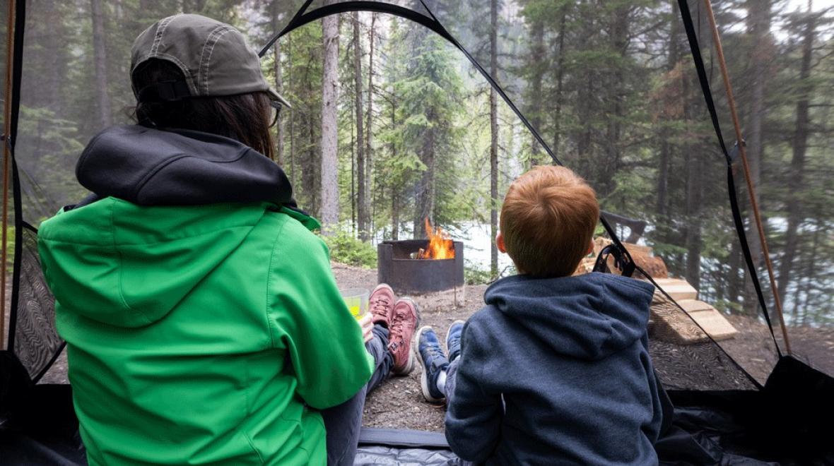 a mother and son sit in a tent looking at a fire at a washington state campground for families in Camano Island