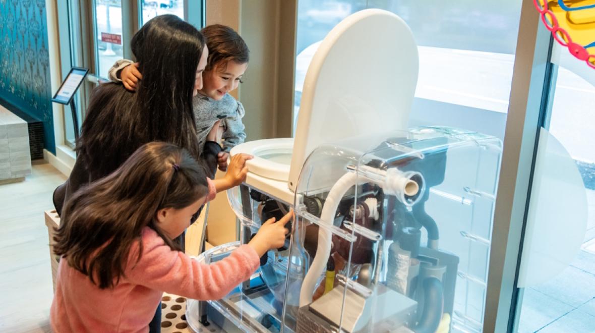 Mom and kids learning how a toilet works at the new exhibit at the Gates Foundation Discovery Center