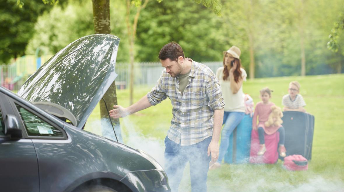 Smoke floats out from under a car hood while a stressed family looks on.
