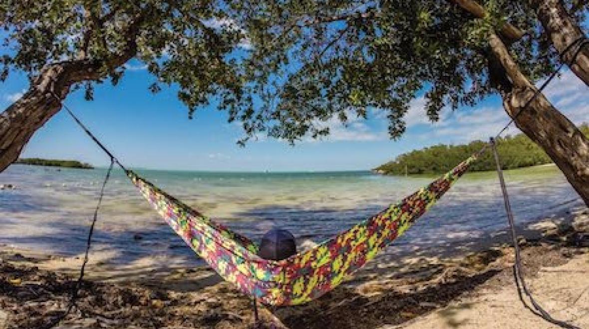 A person relaxes on the beach in a camo ENO hammock.