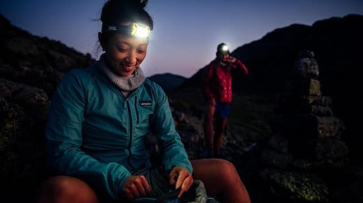 A woman smiles outside at night wearing a PETZL headlamp.