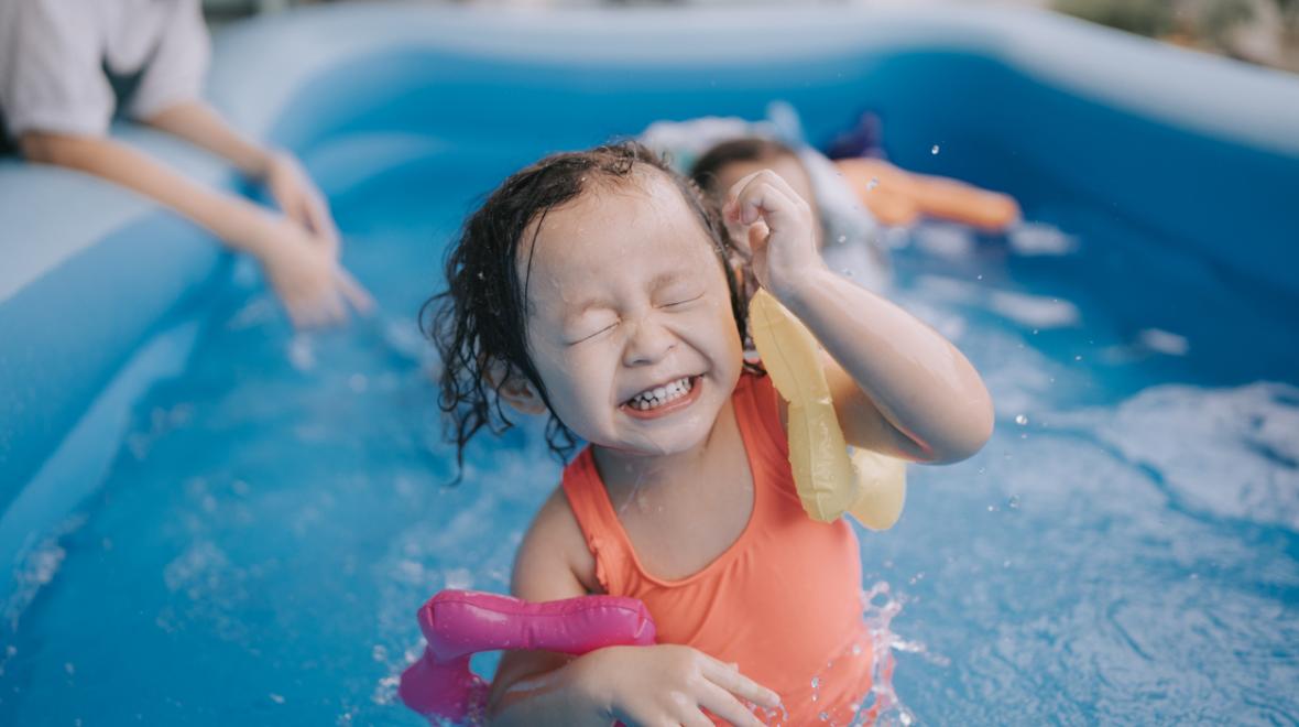 Child smiles while playing in an inflatable pool.