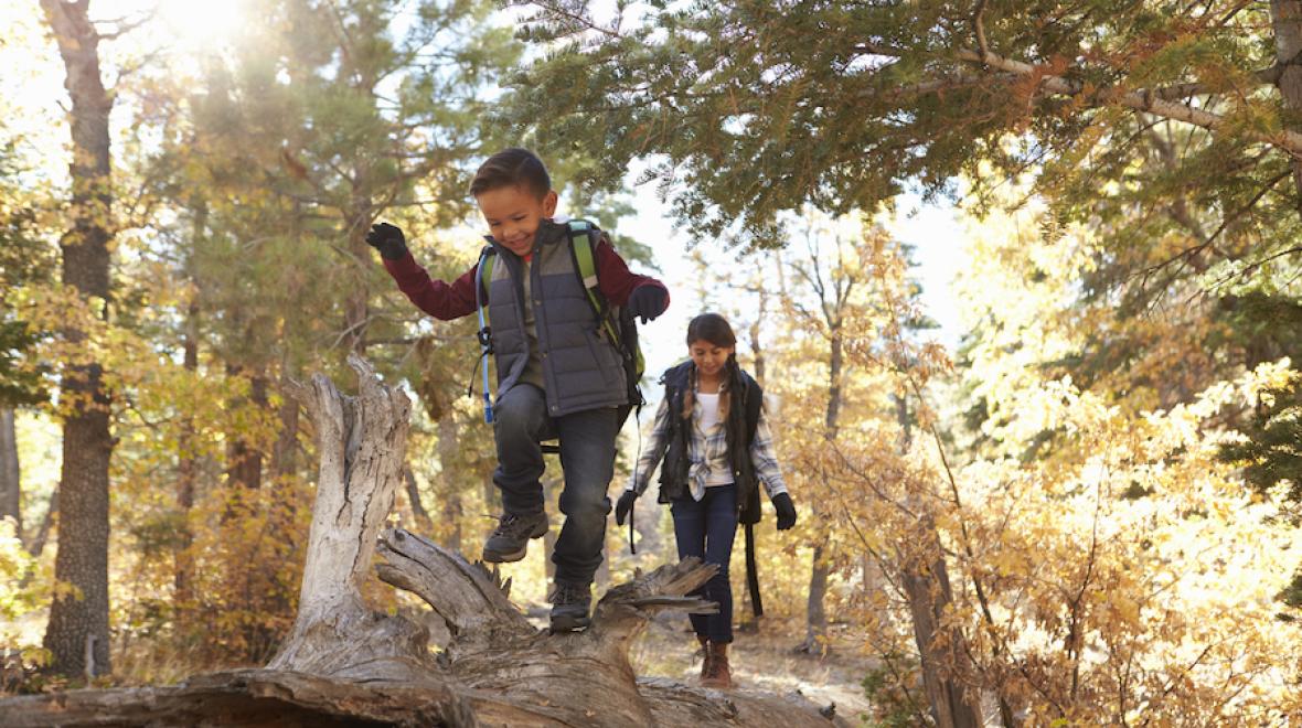 Two children hike with backpacks on while the sun is rising.