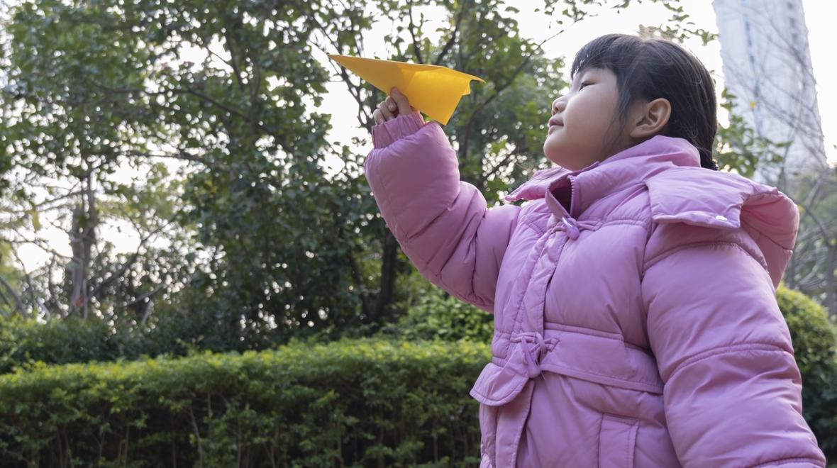 Girl in a pink coat throwing a paper airplane