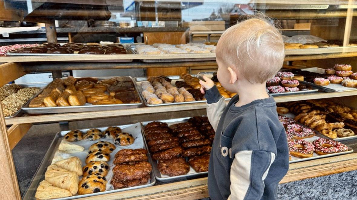a young boy picks out a sweet treat at a donut shop during mid-winter break
