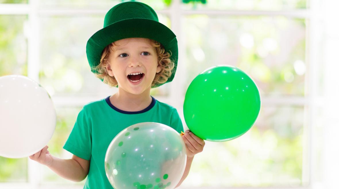 child wearing a hat and green balloons 