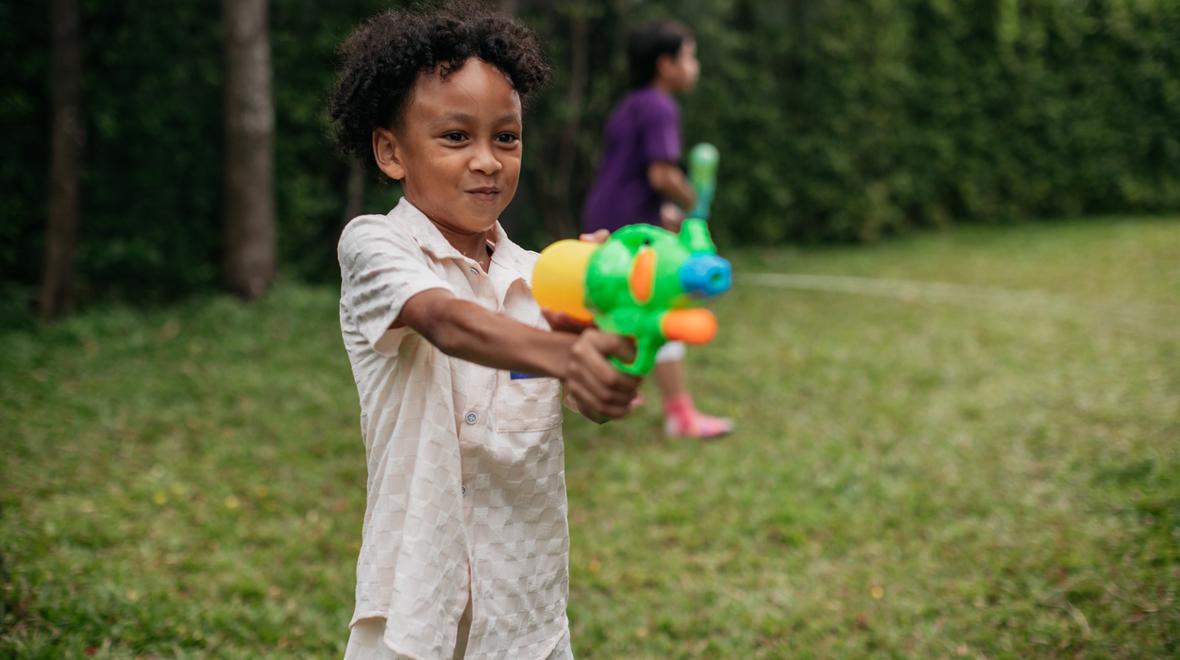 boy aiming a water squirter at a target outside in the summer