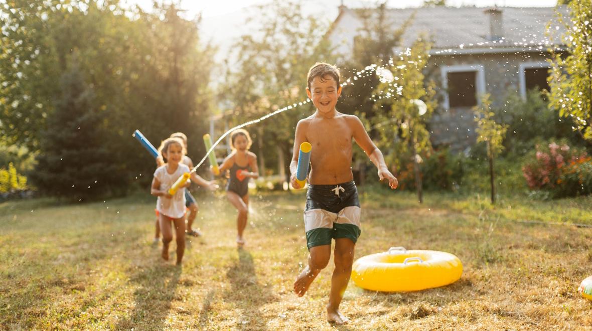 Kids playing with squirt toys outside in the backyard during summer