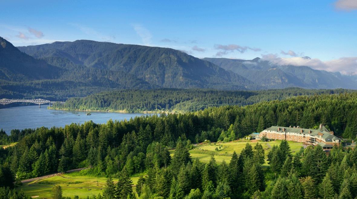 aerial view of the exterior of Skamania Lodge, nestled in the forest with mountains behind it
