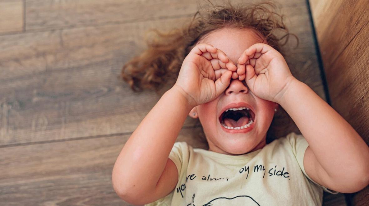 a young girl crying on the floor with hands over eyes after getting home from school and having a tantrum