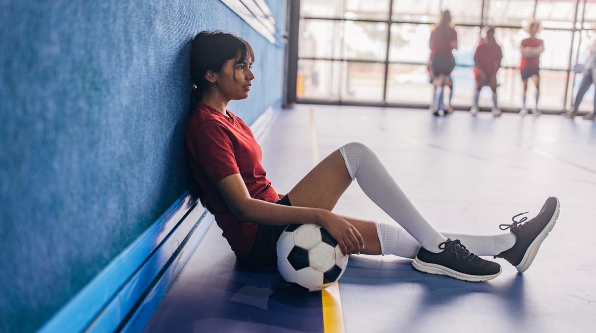girl sitting down in a gym with soccer ball