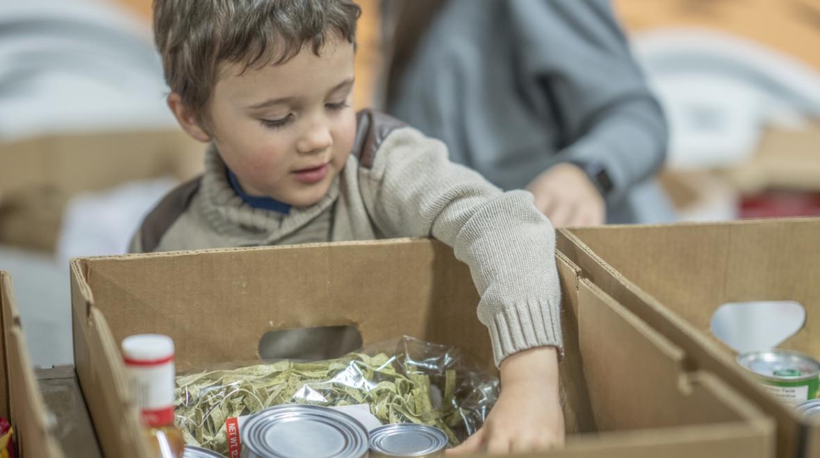 young boy putting food in a box at a food bank