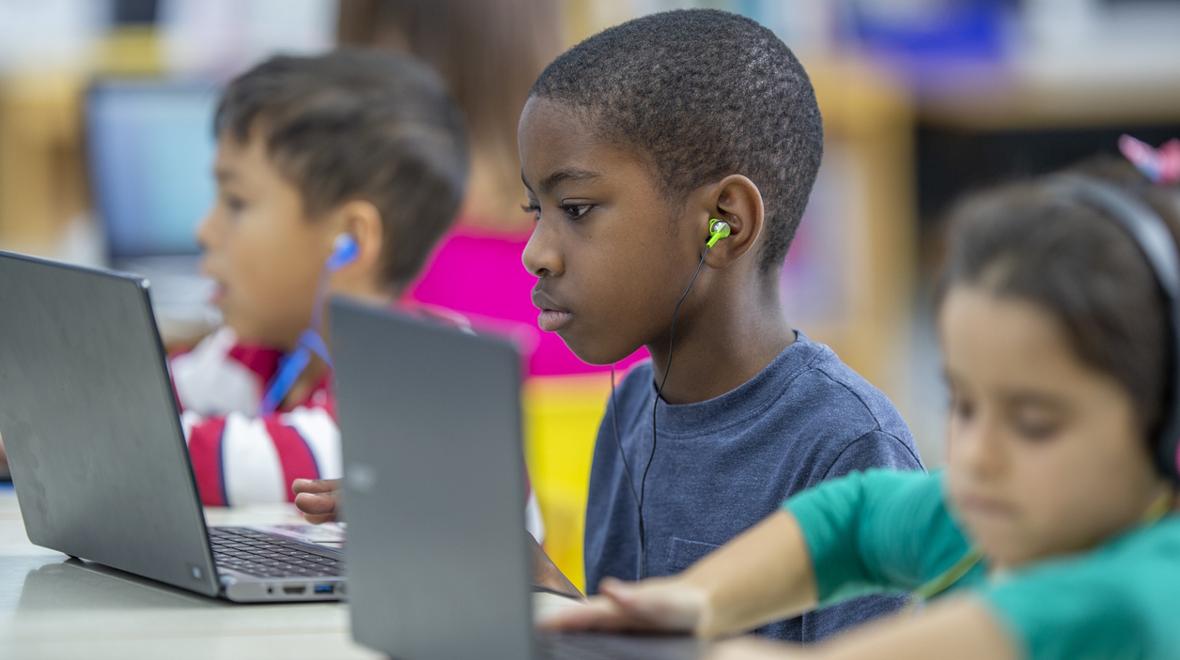boy using a computer and ear buds in a classroom