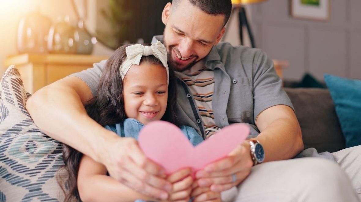 Dad and daughter holding fathers day card on sofa