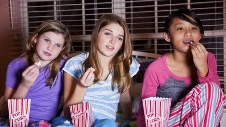 Three girls in pjs eating popcorn and watching a movie