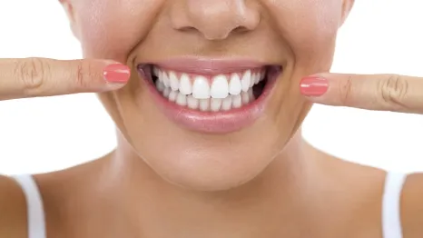 Woman smiling and pointing at her white, healthy teeth