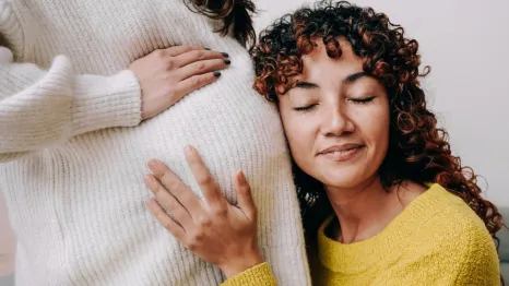 woman cradling partner's pregnant belly and smiling with eyes closed