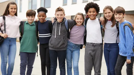 Group of tween kids standing in a line with their arms around each other smiling