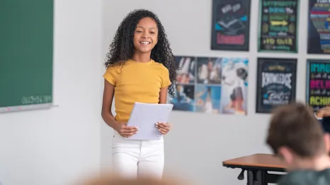 Girl standing in front of her classroom giving a speech and looking confident