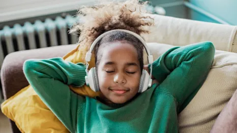 Young girl lying on a couch with eyes closed wearing headphones listening to a best podcasts for kids