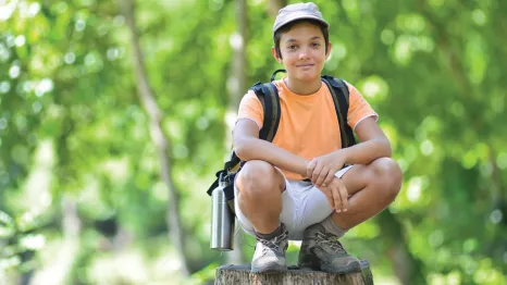 Boy sitting on a rock in the forest at a one-day or drop in Summer camp 