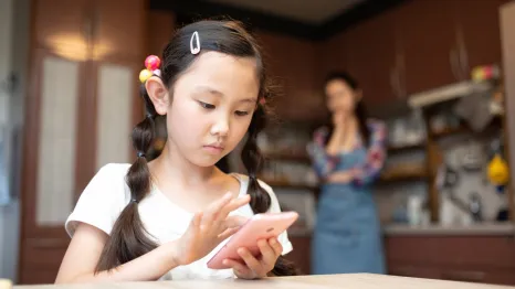 girl using cell phone while mom looks on worried