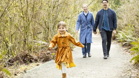 girl walking down a path with mom and dad holding hands behind her