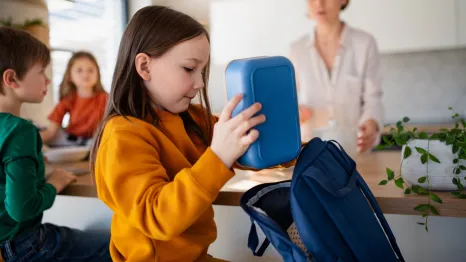 girl putting a lunchbox in her backpack