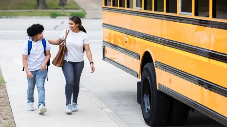 mom and son walking home after school next to a yellow school bus