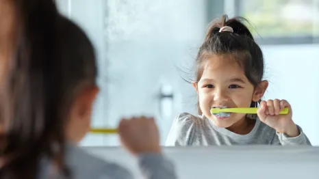 a little girl brushes her teeth in the mirror using tricks that helped her build a new habit