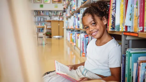 little girl sitting in the library reading a book