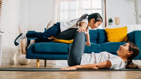 mom doing yoga on the floor with her daughter balancing on her extended legs