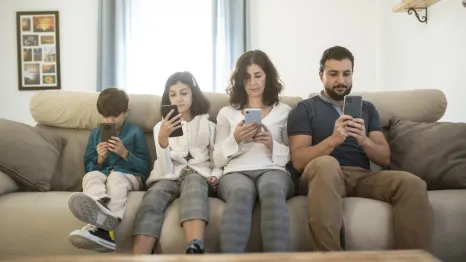 family sitting on a couch looking at their cell phones