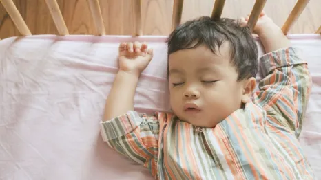 Little boy toddler adorably sleeping in his baby cot