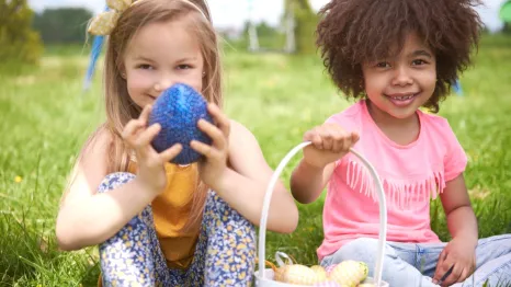 Two girls sitting on grass, holding eggs and basket for Easter.