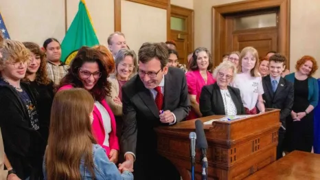 Gov. Bob Ferguson handing over his pen to a child