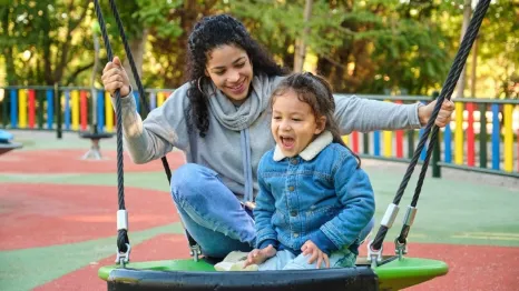 mom playing with child on swing at playground