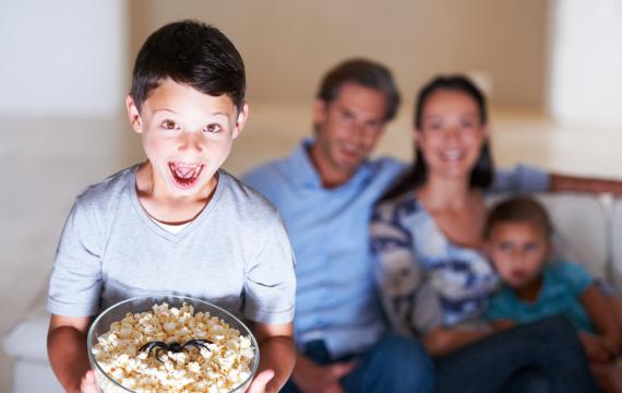 boy holding a bowl of popcorn with a plastic spider in it with his family on the couch in the background