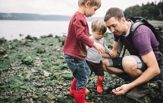 Dad and two little kids looking at rocky beach and tide pool finds at a Seattle beach