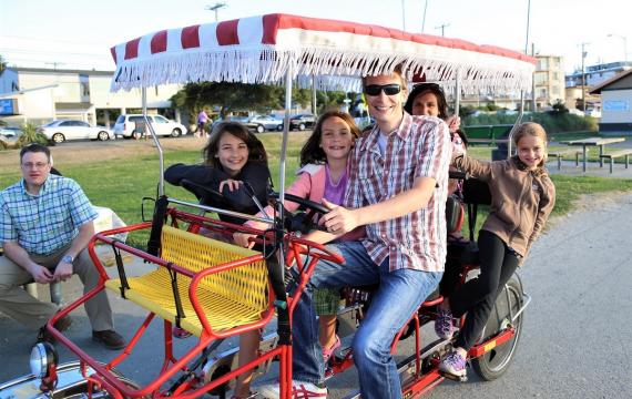 Family riding a surrey-style carriage bike along Alki Beach in Seattle best family activities to celebrate summer with kids