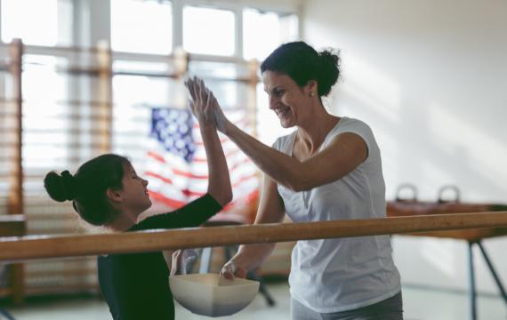 Cute little girl practicing gymnastics and giving her coach a high-five