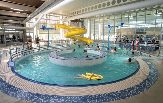 View of people swimming in Rainier Beach Pool in Seattle. Yellow twister slide is in the backgorund and the lazy river feature is in the foreground