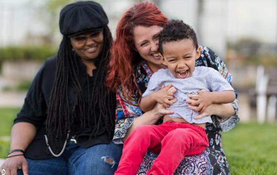 Two women holding a toddler all smiling and laughing