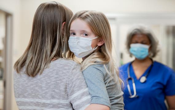 Mom holding young girl wearing mask in a hospital