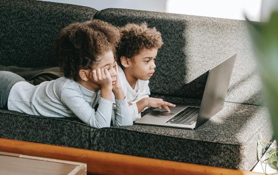 Two young boys lying on a couch looking at a laptop